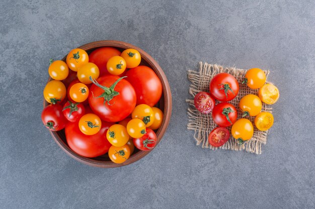 Wooden bowl of colorful organic tomatoes on stone surface