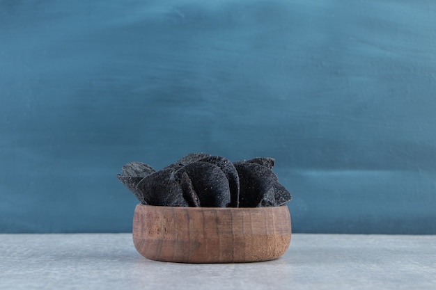 Wooden bowl of crispy black chips on stone.