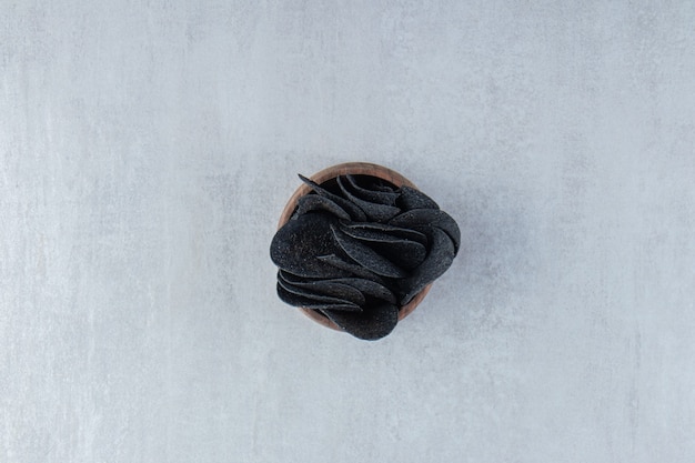 Wooden bowl of crispy black chips on stone.