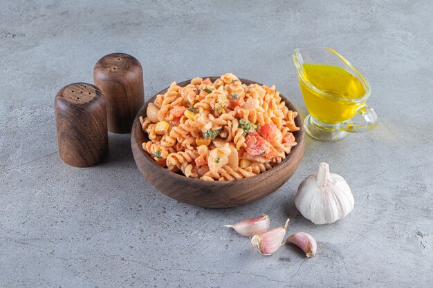 Wooden bowl of delicious fusilli pasta on stone background. 