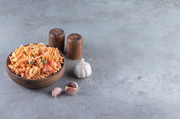 Wooden bowl of delicious fusilli pasta on stone background. 