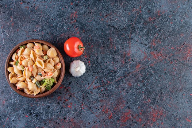 Wooden bowl of delicious seashell pasta on marble surface. 