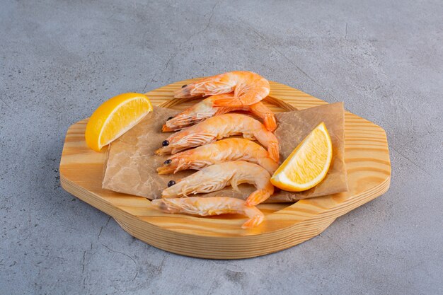 A wooden bowl of delicious shrimps with sliced lemon on a stone background .