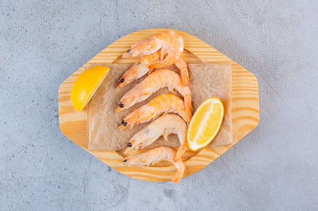 A wooden bowl of delicious shrimps with sliced lemon on a stone surface 