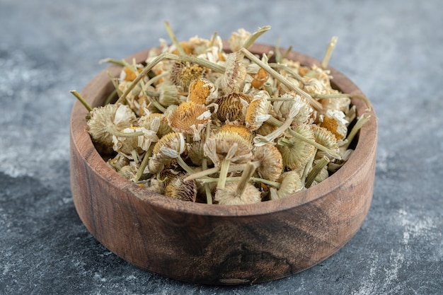 Free photo wooden bowl of dried chamomile on marble table.