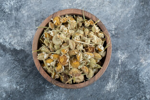 Wooden bowl of dried chamomile on marble table. 