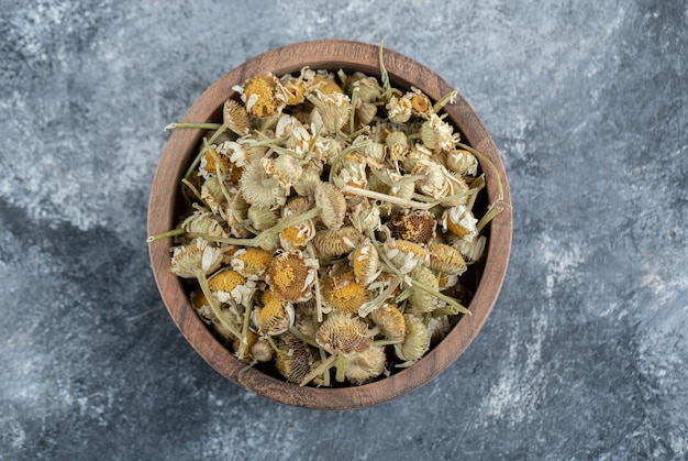 Wooden bowl of dried chamomile on marble table. 