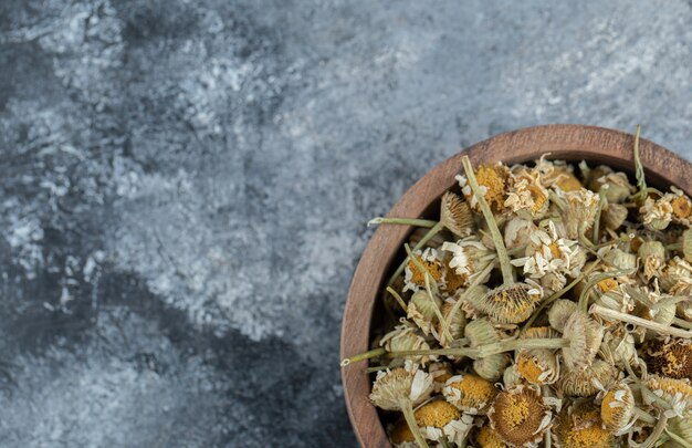 Wooden bowl of dried chamomile on marble table. 