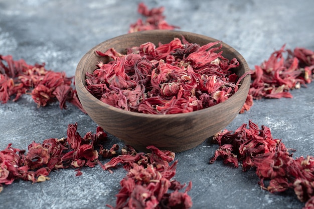 Wooden bowl of dried flower petals on marble table.