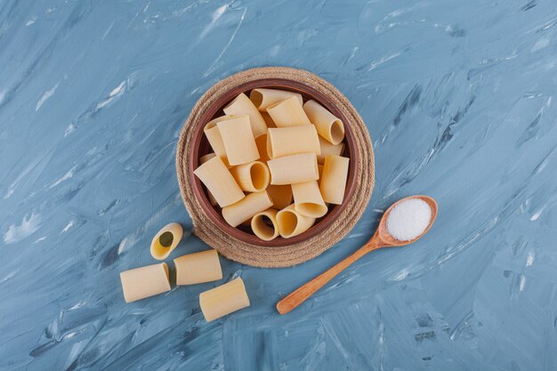 A wooden bowl of dry raw tube pasta on a blue table.