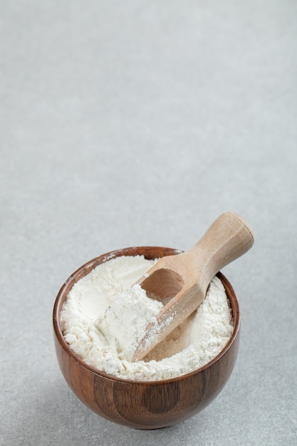 A wooden bowl of flour and wooden spoon on marble surface.