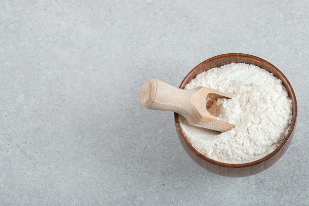 A wooden bowl of flour and wooden spoon .