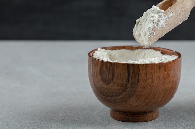 A wooden bowl of flour and wooden spoon .