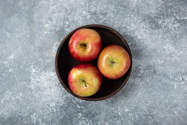 Wooden bowl of fresh bright apples on marble surface.