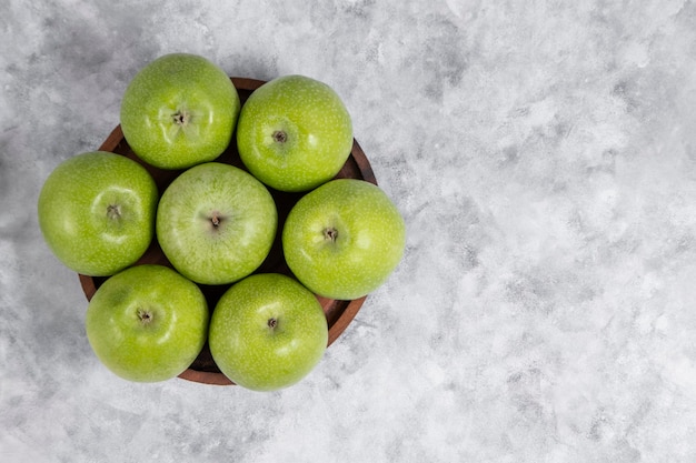 A wooden bowl of fresh green sweet apples on stone