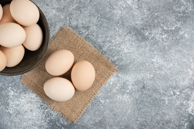 Wooden bowl of fresh organic raw eggs on marble surface.