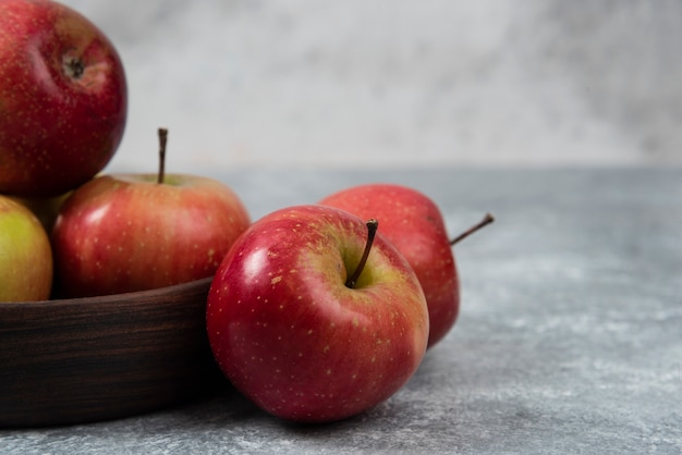 Wooden bowl of fresh tasty apples on marble surface.