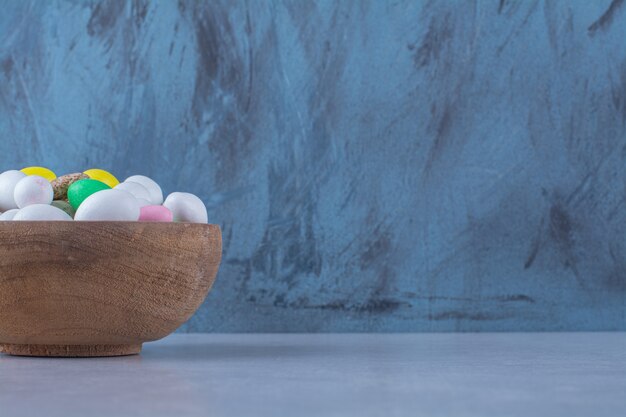 Free photo a wooden bowl full of colorful bean candies on gray surface