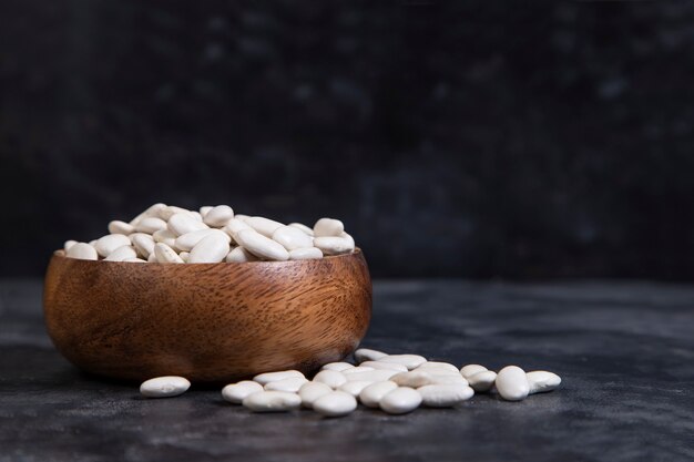 A wooden bowl full of dry butter beans placed on stone