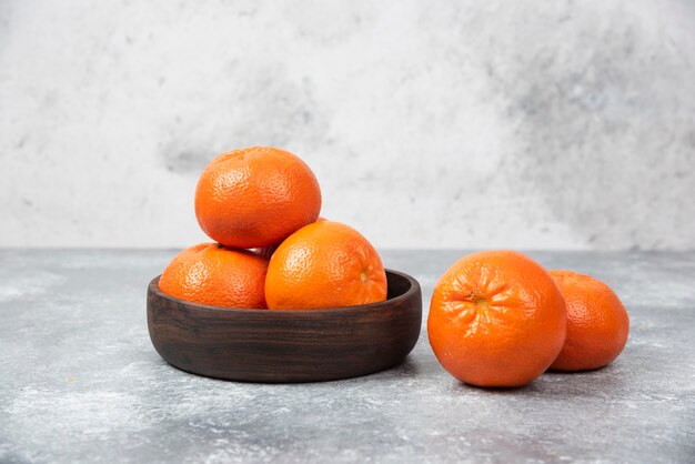 A wooden bowl full of juicy orange fruits on stone table .
