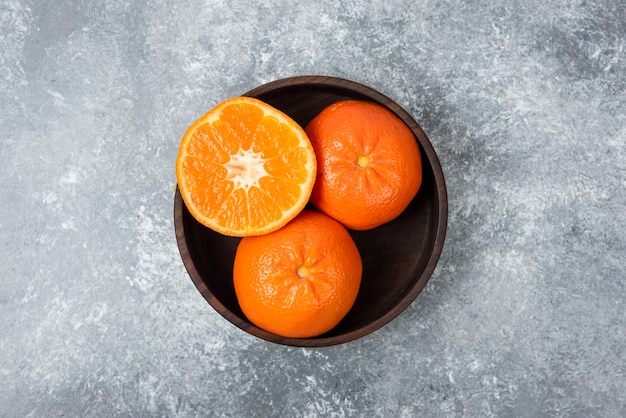 A wooden bowl full of juicy orange fruits on stone table .