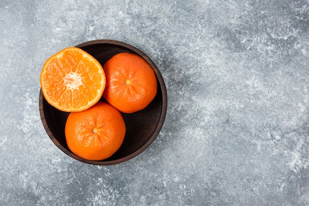 A wooden bowl full of juicy orange fruits on stone table .