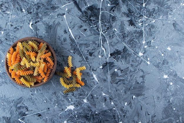 A wooden bowl full of multi colored macaroni on a gray background . 