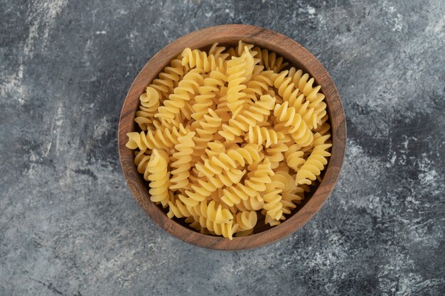 A wooden bowl full of raw dry fusilli pasta . 