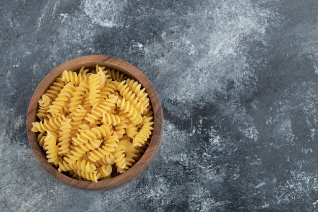 A wooden bowl full of raw dry fusilli pasta . 