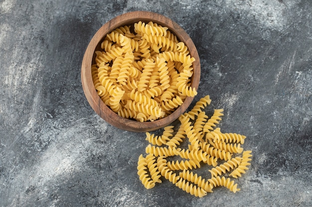 A wooden bowl full of raw dry Fusilli pasta. 