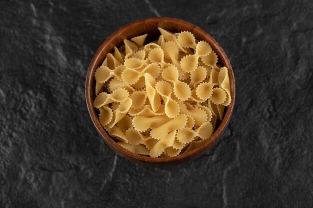 A wooden bowl full of raw farfalle tonde macaroni . 