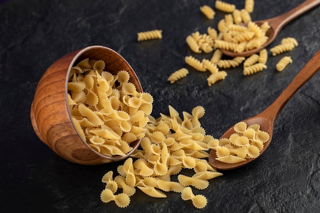 A wooden bowl full of raw farfalle tonde macaroni . 