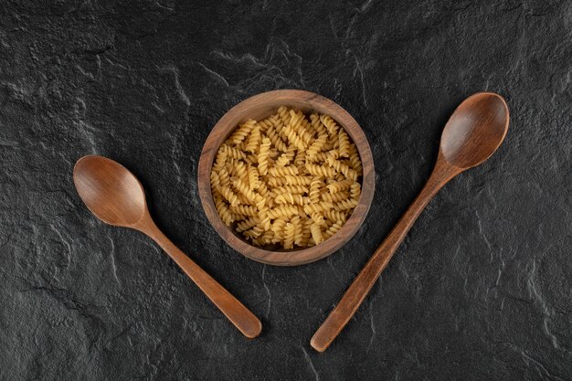 A wooden bowl full of raw girandole pasta . 