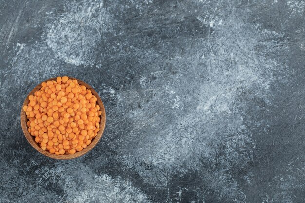 A wooden bowl full of raw lentils on gray.