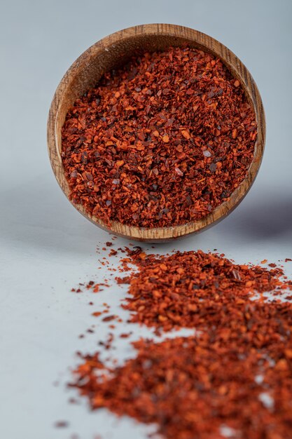 A wooden bowl full of red pepper on a white surface .