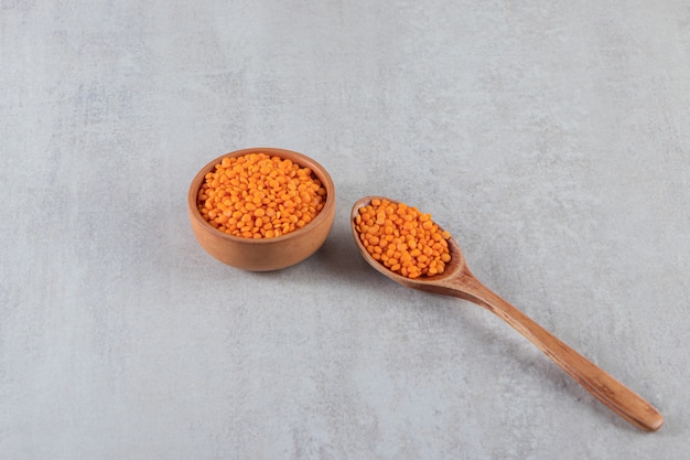 Free photo wooden bowl full of red raw lentils on stone background.
