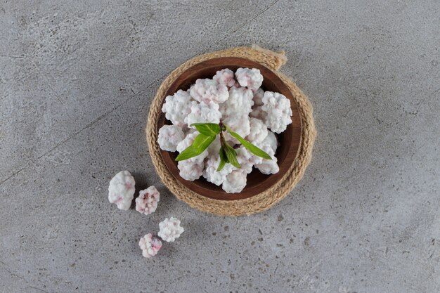 A wooden bowl full of sweet white candies with mint leaves on a stone table . 
