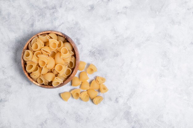 Wooden bowl full of uncooked pasta Conchiglie placed on marble background . High quality photo