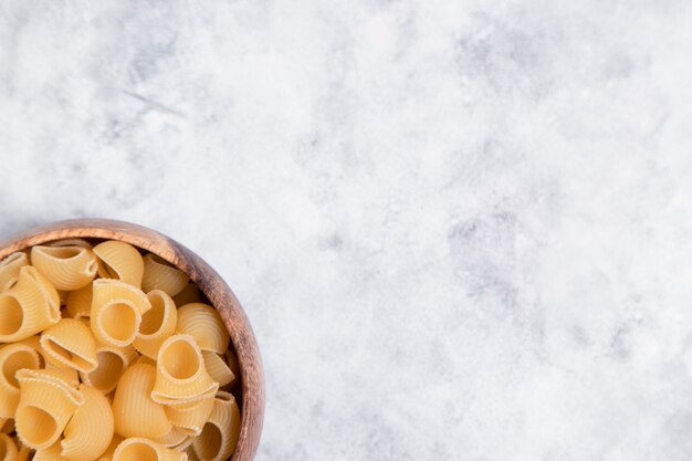 Wooden bowl full of uncooked pasta Conchiglie placed on marble background . High quality photo