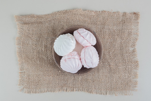 Free photo a wooden bowl full of white and pink zephyrs .