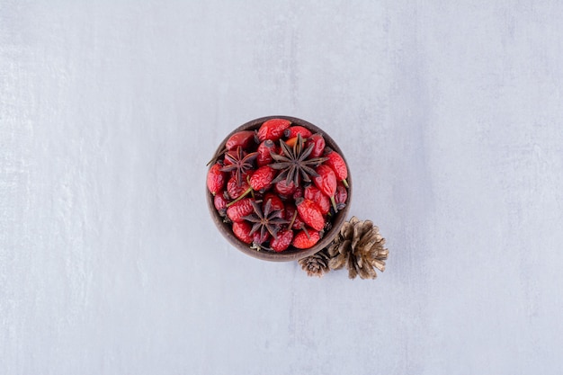 Free photo wooden bowl of hips and anise next to pine cones on white background.