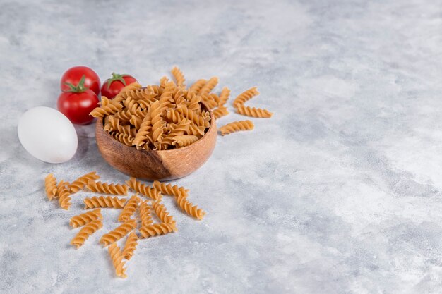 Деревянная миска итальянской сырой сухой пасты Fusilli rigate с помидорами. Фото высокого качества