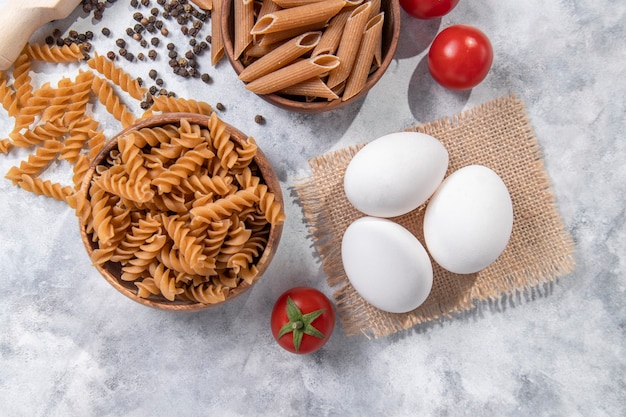 A wooden bowl of Italian uncooked dry pasta Fusilli with pepper corns . High quality photo