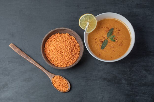 A wooden bowl of lentil beans with soup and slice of lemon .