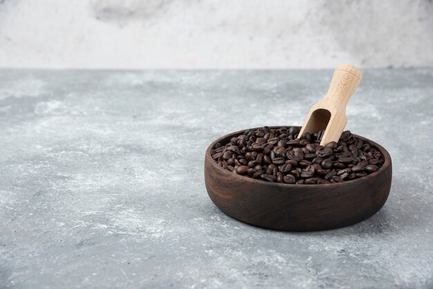 Wooden bowl of medium roasted coffee with spoon on marble surface.