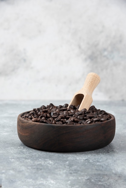 Wooden bowl of medium roasted coffee with spoon on marble surface.