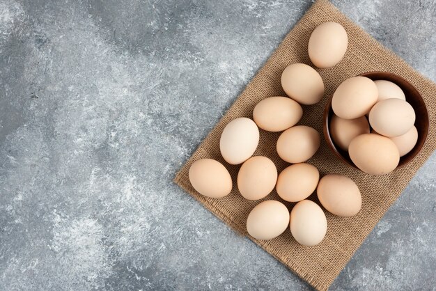 Wooden bowl of organic raw eggs on marble surface.