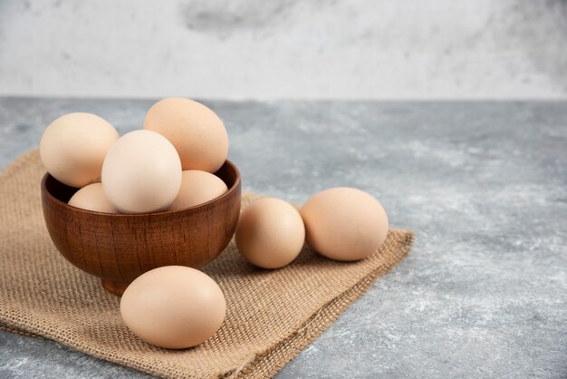 Wooden bowl of organic raw eggs on marble surface.