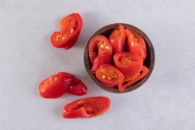 Wooden bowl of pickled tomatoes placed on stone table.