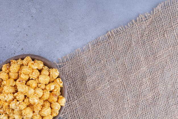 Wooden bowl on a piece of fabric with a pile of caramel popcorn on marble surface